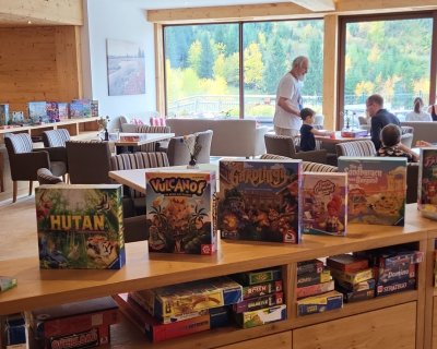 Brettspiele auf Regal aufgestellt im Hintergrund spielt eine Gruppe auf einem Tisch