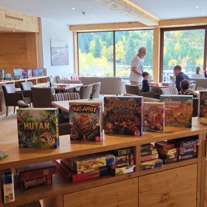 Brettspiele auf Regal aufgestellt im Hintergrund spielt eine Gruppe auf einem Tisch