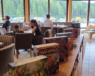 Brettspiele auf Regal aufgestellt im Hintergrund spielt eine Gruppe auf einem Tisch