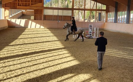 Mädchen reitet auf Pferd in einer Reithalle mit einem Reitlehrer