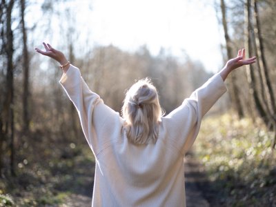 Frau hält die Hände in die Höhe und steht im Wald