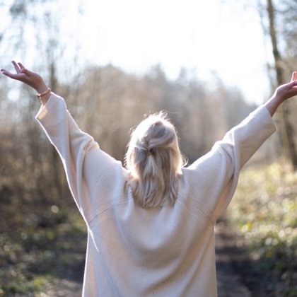 Frau hält die Hände in die Höhe und steht im Wald