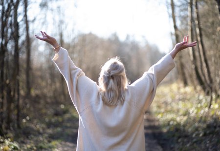Frau hält die Hände in die Höhe und steht im Wald
