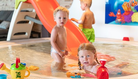 Drei Kleinkinder spielen im flachen Becken mit Rutsche und Spielzeug