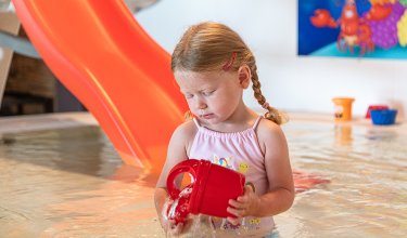 Mädchen gießt Wasser aus roter Kanne im Kinderbecken