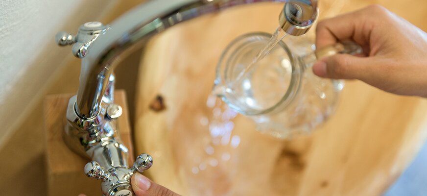 Wasser fließt aus dem Trinkhahn in einen Krug