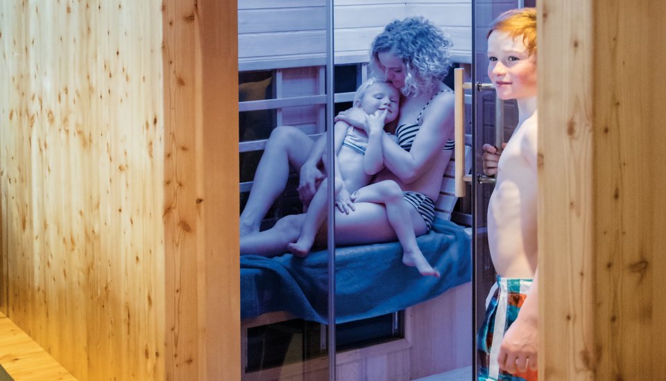 Mother cuddling child in infrared cabin, boy entering the room