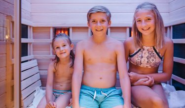 Drei lächelnde Kinder sitzen in einer Infrarotsauna