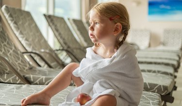 Toddler in bathrobe with apple on lounger in relaxation area