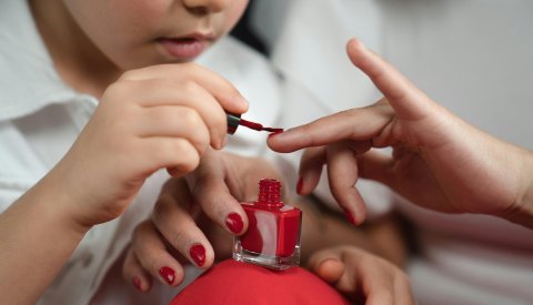 Kind lackiert Nägel mit rotem Nagellack.