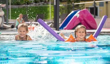 Zwei Mädchen spielen mit Poolnudeln im Kinderbecken