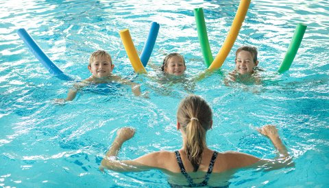 Kinder lernen schwimmen mit Poolnudeln und Lehrerin im Hallenbad