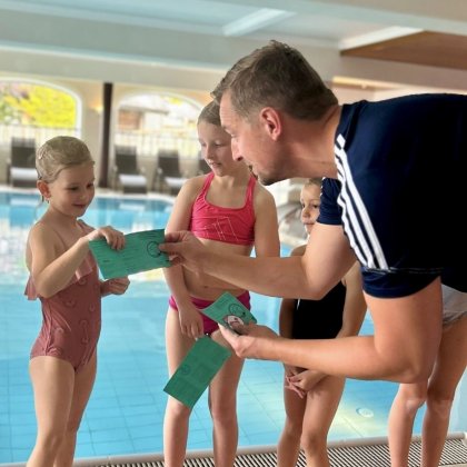 Mann übergibt Kindern am Hallenbad grüne Schwimmausweise