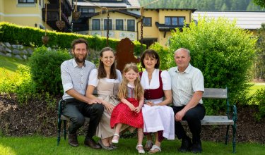 Familie in Tracht auf einer Gartenbank vor dem Hotel
