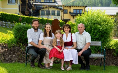 Familie in Tracht auf einer Gartenbank vor dem Hotel