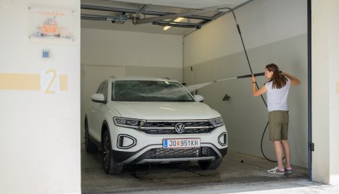 Frau reinigt weißen SUV mit Hochdruckreiniger in Waschbox