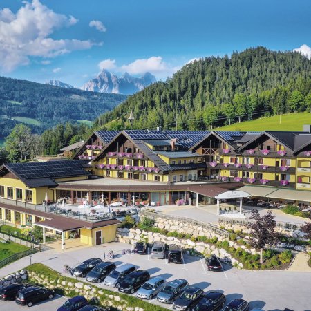 Hotel mit gelber Fassade, Blumendekor und Bergpanorama im Hintergrund