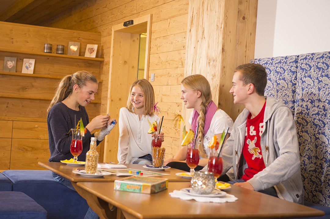 Vier Jugendliche spielen Activity und trinken bunte Cocktails im Spielraum