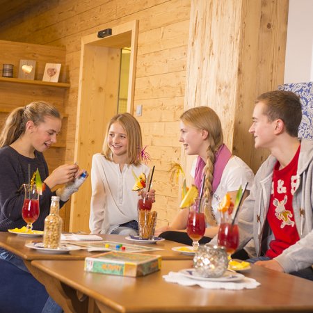 Vier Jugendliche spielen Activity und trinken bunte Cocktails im Spielraum