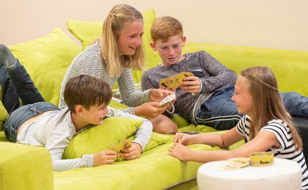 Vier Kinder spielen lachend Karten auf einem grünen Sofa