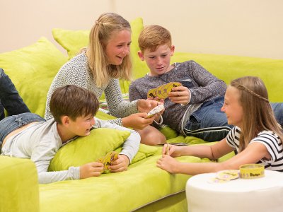 Vier Kinder spielen lachend Karten auf einem grünen Sofa