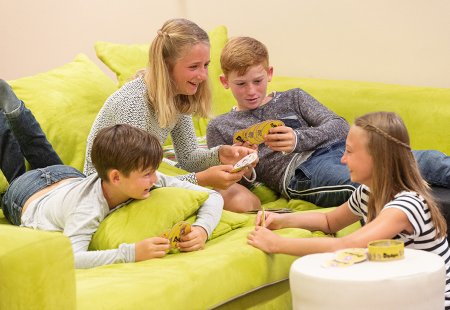 Vier Kinder spielen lachend Karten auf einem grünen Sofa