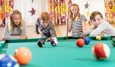 Vier Kinder beim konzentrierten Billardspiel im farbenfrohen Spielraum