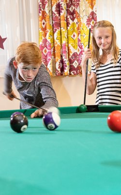 Vier Kinder beim konzentrierten Billardspiel im farbenfrohen Spielraum