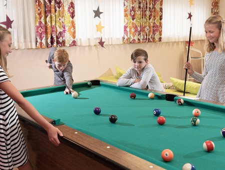 Vier Kinder spielen gemeinsam Billard in einem bunt dekorierten Raum