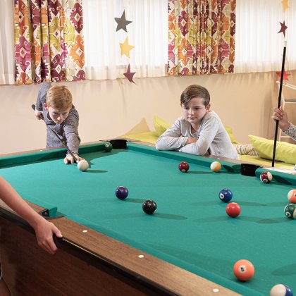 Vier Kinder spielen gemeinsam Billard in einem bunt dekorierten Raum