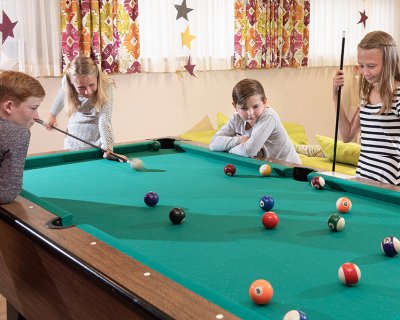 Vier Kinder spielen gemeinsam Billard in einem bunt dekorierten Raum