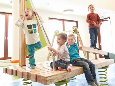Kinder spielen lachend auf einem hölzernen Spiel-Floß im Indoorbereich