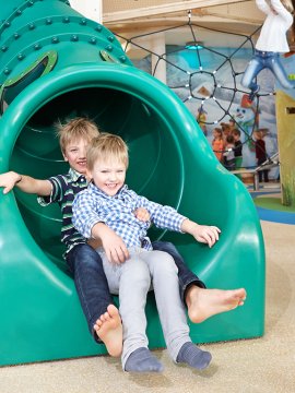 Zwei Buben rutschen lachend die grüne Röhrenrutsche im Indoorspielplatz hinunter