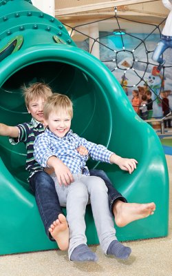 Zwei Buben rutschen lachend die grüne Röhrenrutsche im Indoorspielplatz hinunter