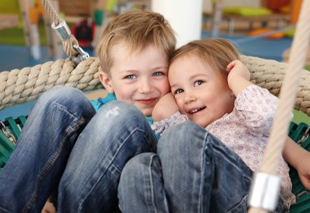 Zwei Kinder kuscheln in Netzschaukel in heller Indoor-Spielwelt