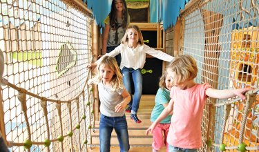 Kinder balancieren lachend über eine Hängebrücke im Indoor-Spielbereich