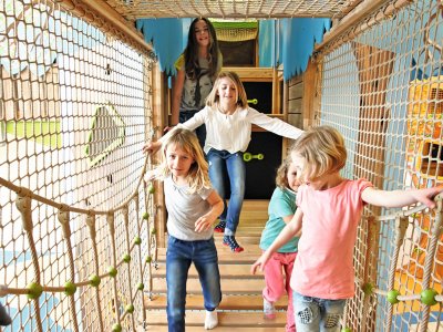 Kinder balancieren lachend über eine Hängebrücke im Indoor-Spielbereich
