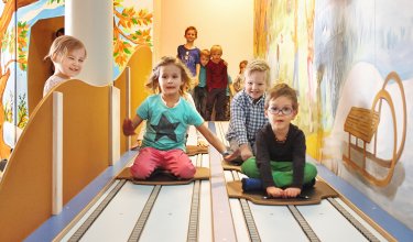 Kinder rodeln lachend auf der Indoor-Bahn mit bunter Wandmalerei