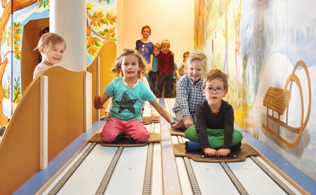 Kinder rodeln lachend auf der Indoor-Bahn mit bunter Wandmalerei