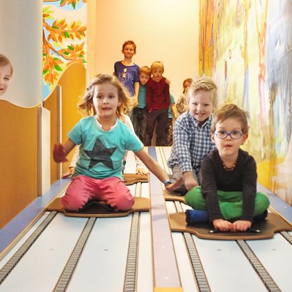 Kinder rodeln lachend auf der Indoor-Bahn mit bunter Wandmalerei