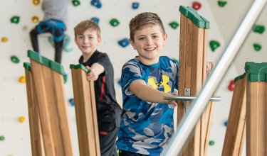 Junge balancieren auf Holzstelzen vor bunter Kletterwand