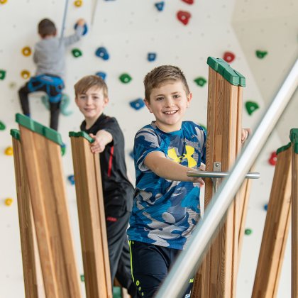 Junge balancieren auf Holzstelzen vor bunter Kletterwand