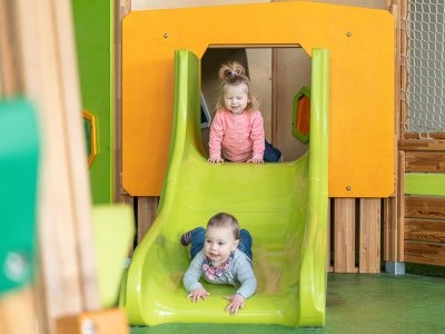 Zwei Kleinkinder rutschen nacheinander die grüne Rutsche hinunter