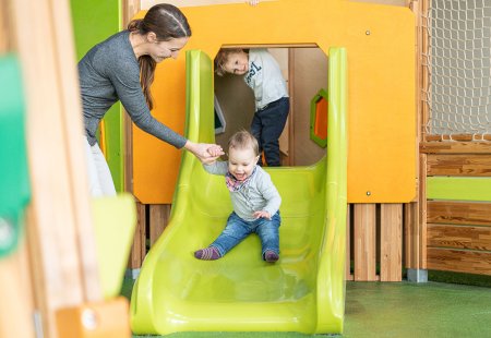 Kleinkind rutscht mit Unterstützung der Mutter die grüne Rutsche hinunter