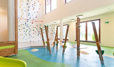 Helle Indoor-Kletterwand mit bunten Griffen und Balancierbereich