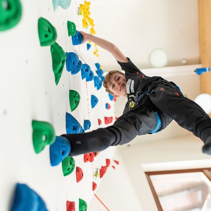 Junge beim Klettern an einer bunten Indoor-Kletterwand mit Sicherung