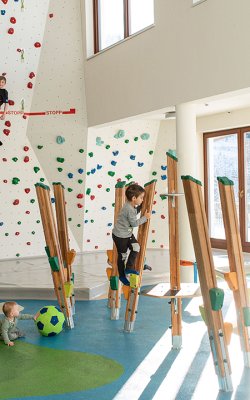 Kinder beim Spielen und Klettern in heller Indoor-Spielhalle mit Boulderwand