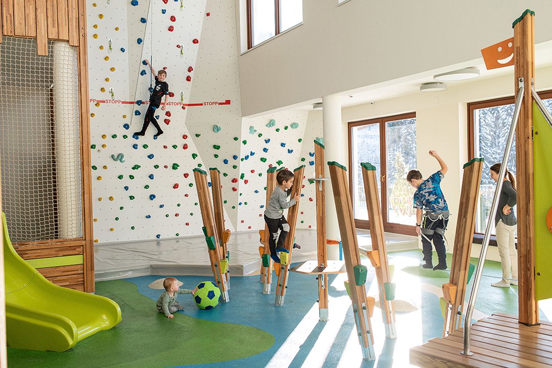 Kinder beim Spielen und Klettern in heller Indoor-Spielhalle mit Boulderwand
