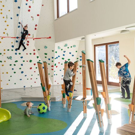 Kinder beim Spielen und Klettern in heller Indoor-Spielhalle mit Boulderwand