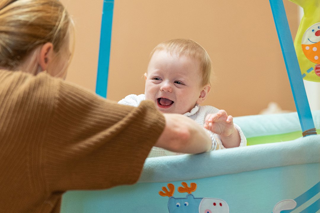 Baby spielt lachend mit Frau in hellblauer Hängeschale mit Tiermotiven